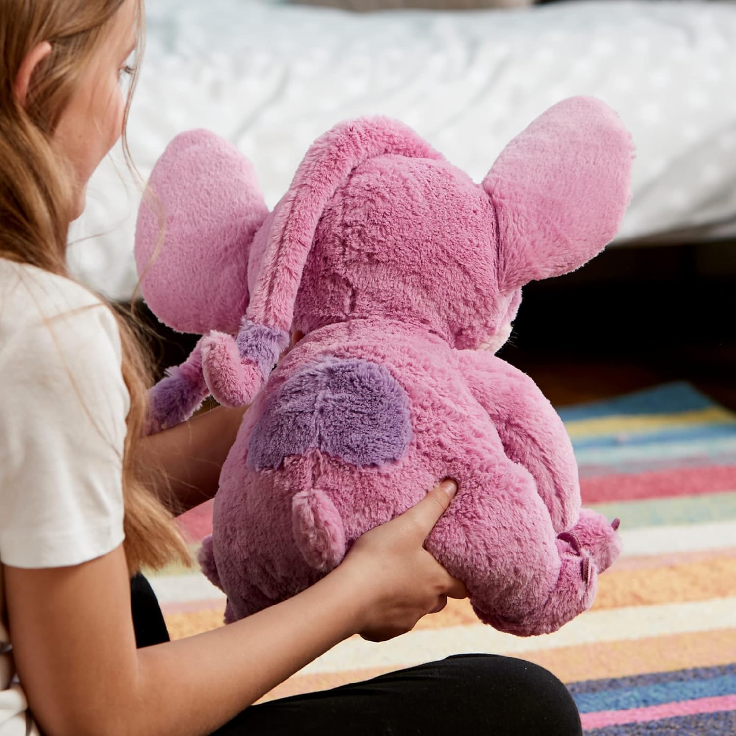 Child holding Disney Angel plush toy from the back, showing soft pink texture, floppy ears, and embroidered wings.
