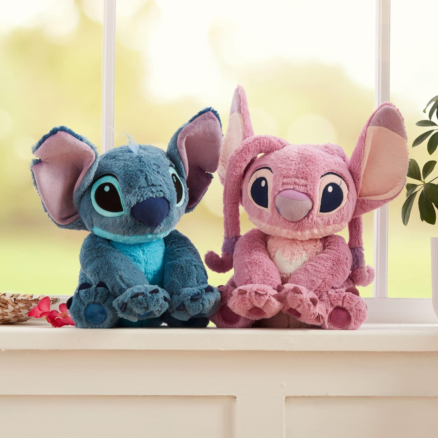 Disney Angel and Stitch medium plush toys sitting side by side near a window, featuring soft fabric and embroidered facial details.