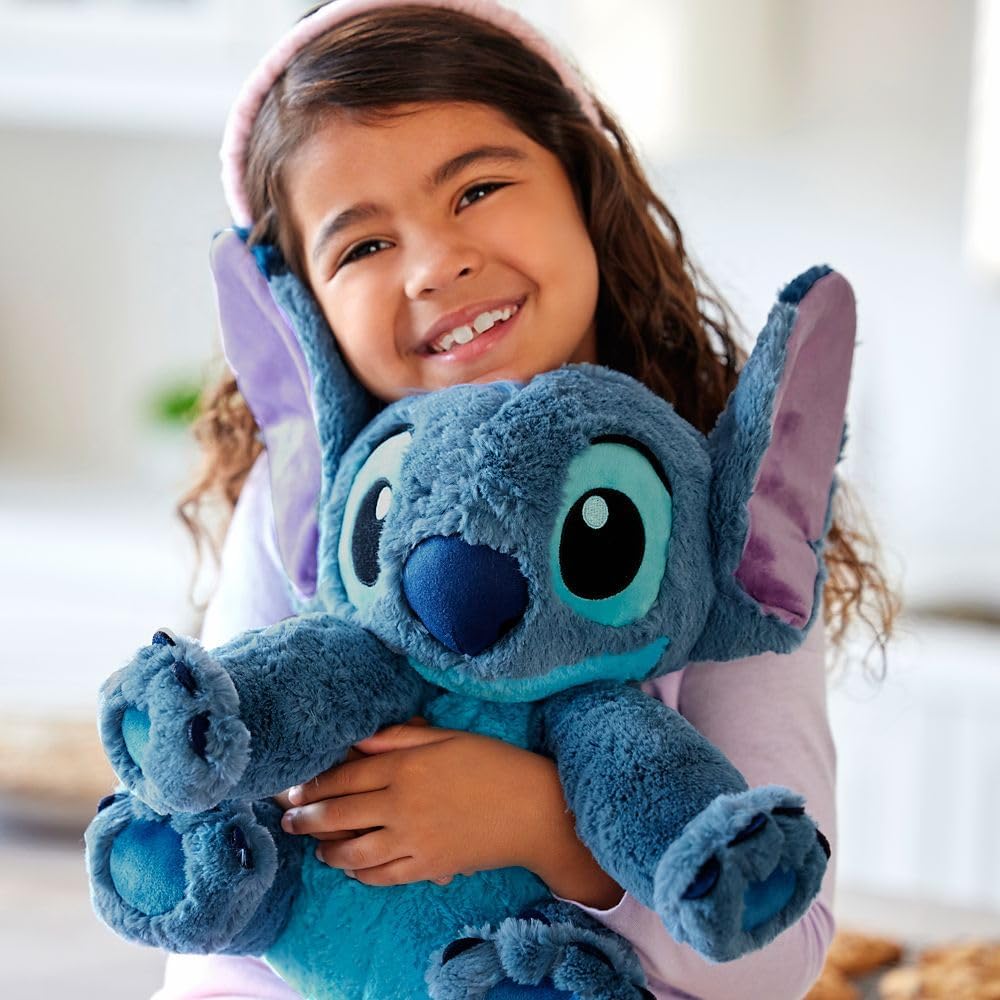 Smiling child hugging Disney Store official Stitch medium soft toy plush with fuzzy blue texture and floppy ears.