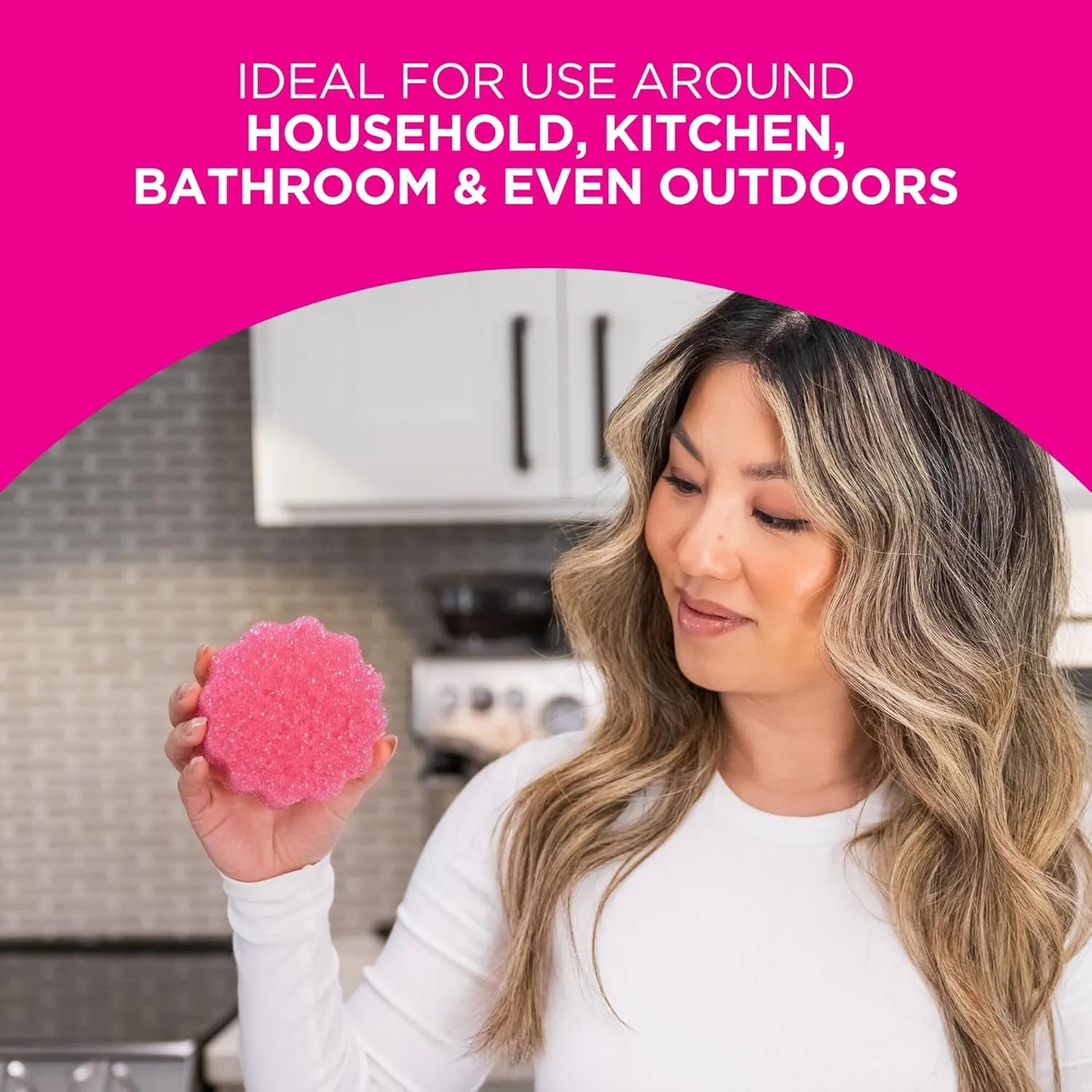 Woman holding Pink Stuff scrubber sponge in kitchen, suitable for household, kitchen, bathroom, and outdoor cleaning.